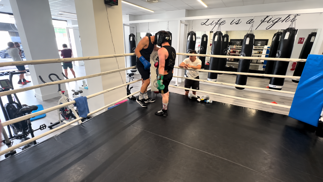 Dos boxeadores escuchan a un entrenador junto a las cuerdas del ring.