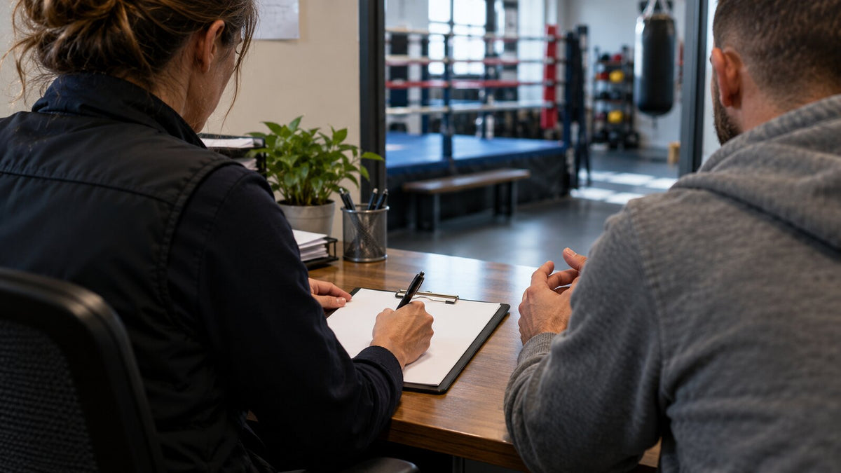 Responsable de bienestar toma notas objetivas durante una conversación confidencial en un gimnasio de boxeo.