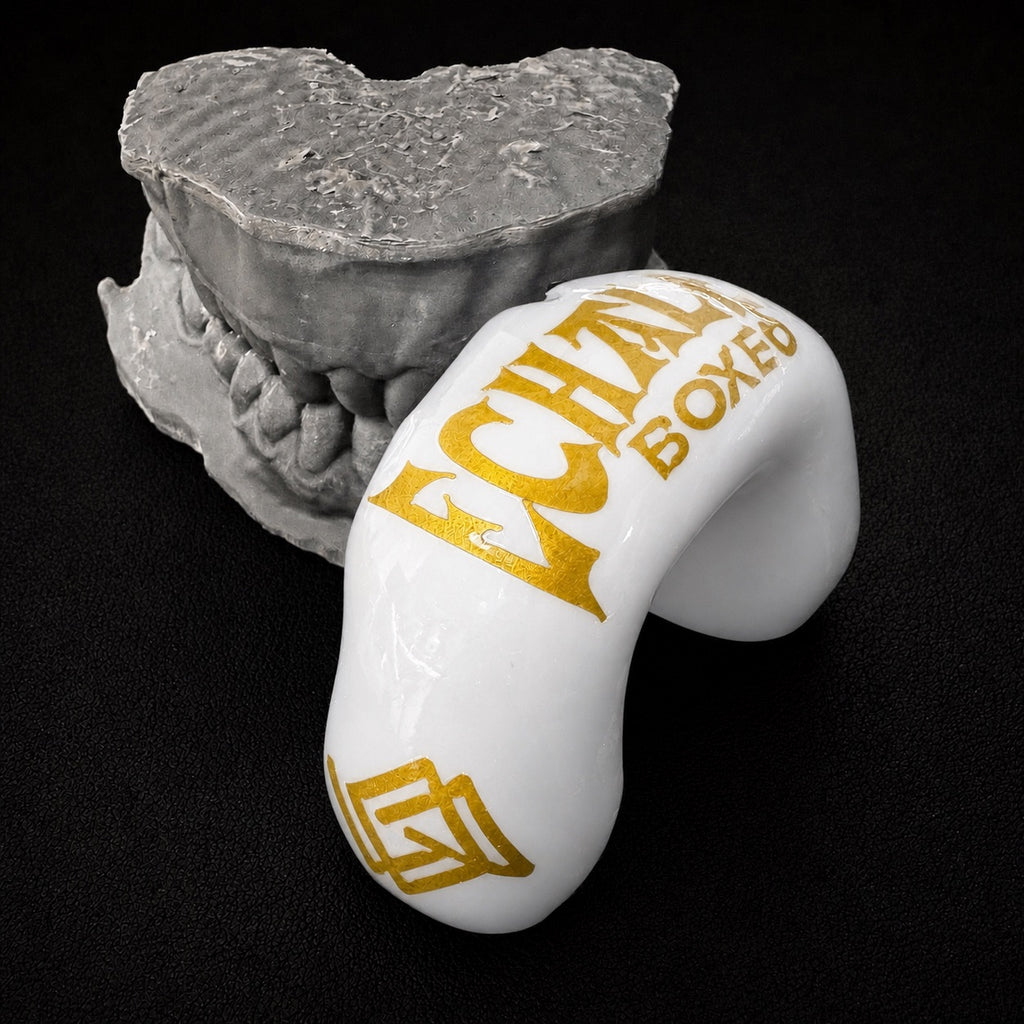 Protector bucal blanco con detalles dorados junto a molde dental gris - Echaleku Boxeo