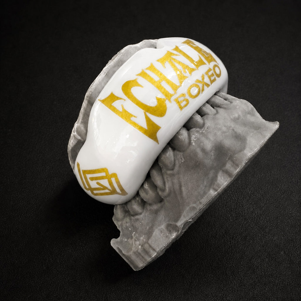 Protector bucal blanco con detalles dorados sobre molde dental gris - Echaleku Boxeo